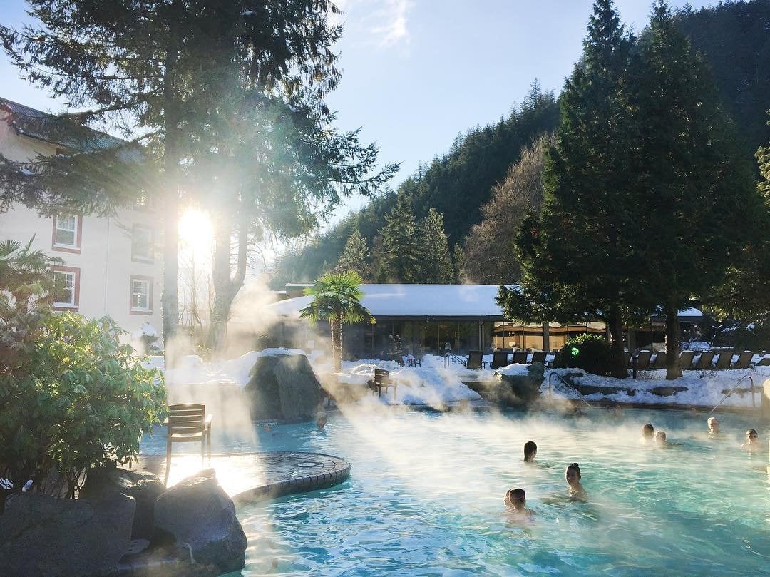 Bathers in an outdoors hot springs pool in the winter time as snow dusts the ground
