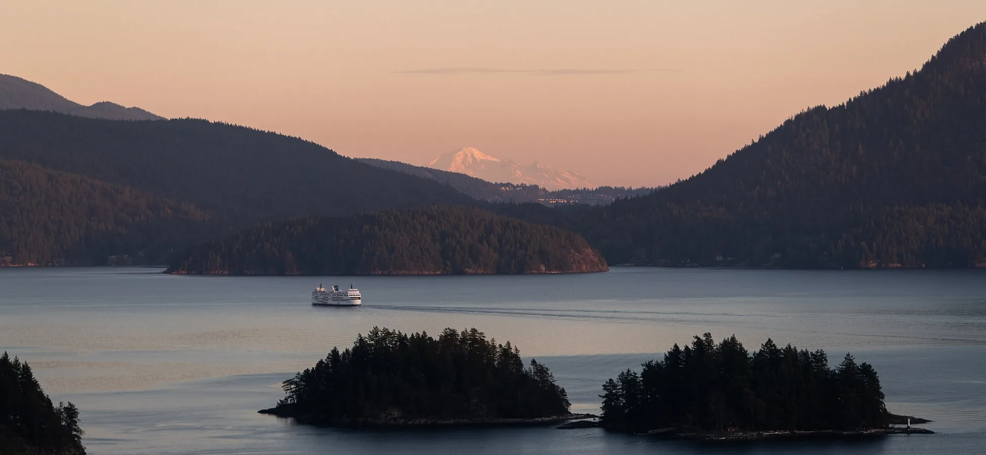 Aerial view of a BC Ferry sailing past two small islands at sunset