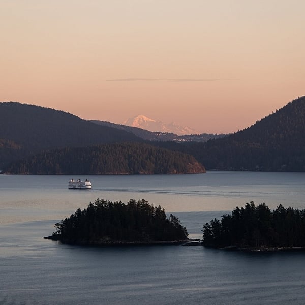 Aerial view of a BC Ferry sailing past two small islands at sunset