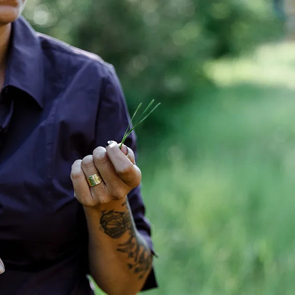 A person is seen holding a piece of grass in their hand (their head is not shown in the frame).