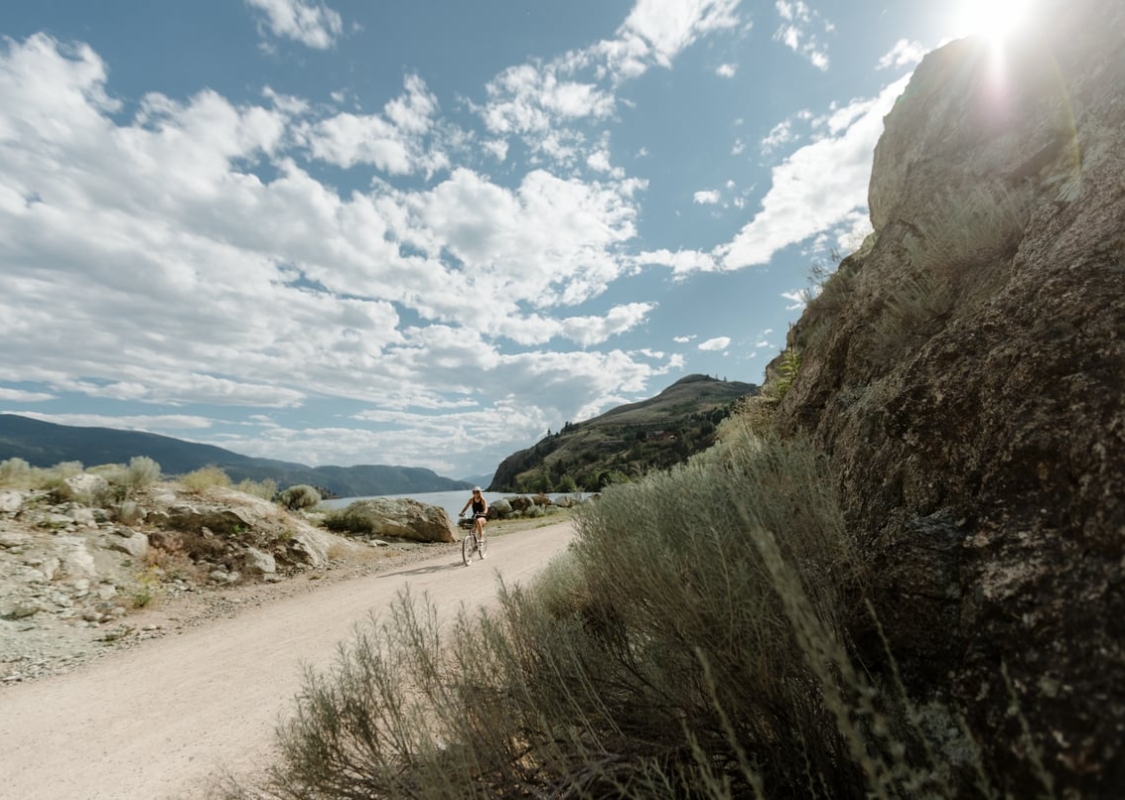 Ein*e Radfahrer*in auf dem Okanagan Rail Trail an einem strahlend sonnigen Tag.