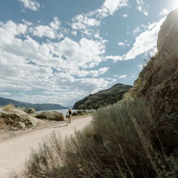 Ein*e Radfahrer*in auf dem Okanagan Rail Trail an einem strahlend sonnigen Tag.