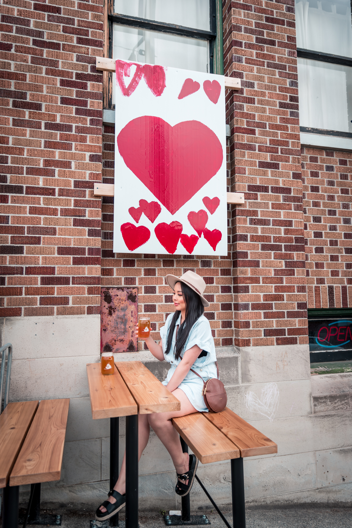 A women sits on a patio at a wooden bench table with a drink in her hand.