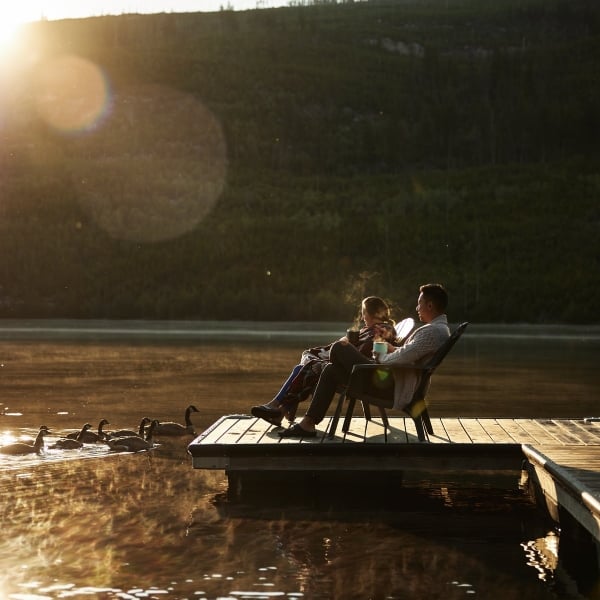 Zwei Personen sitzen bei Sonnenuntergang auf einem Steg an der Chuta Lake Lodge.
