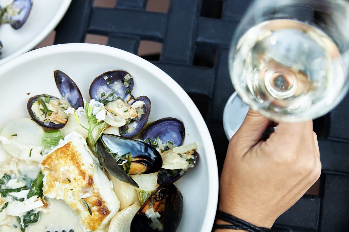 A plate of mussels and other seafood, and a glass of wine on a table.