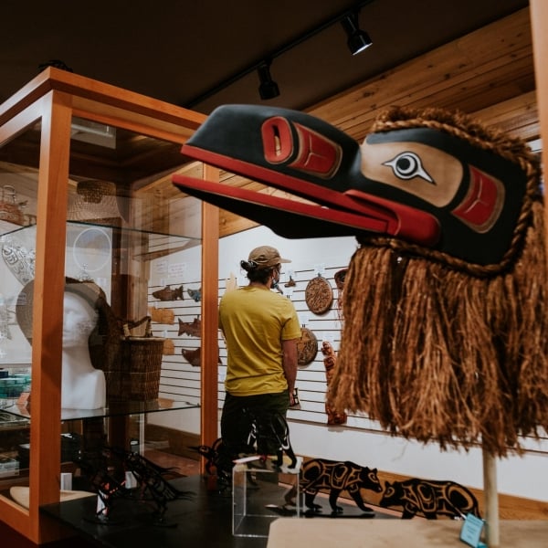 A collection of Indigenous art in glass cases and on the walls. A man examines a piece on the wall in the background.