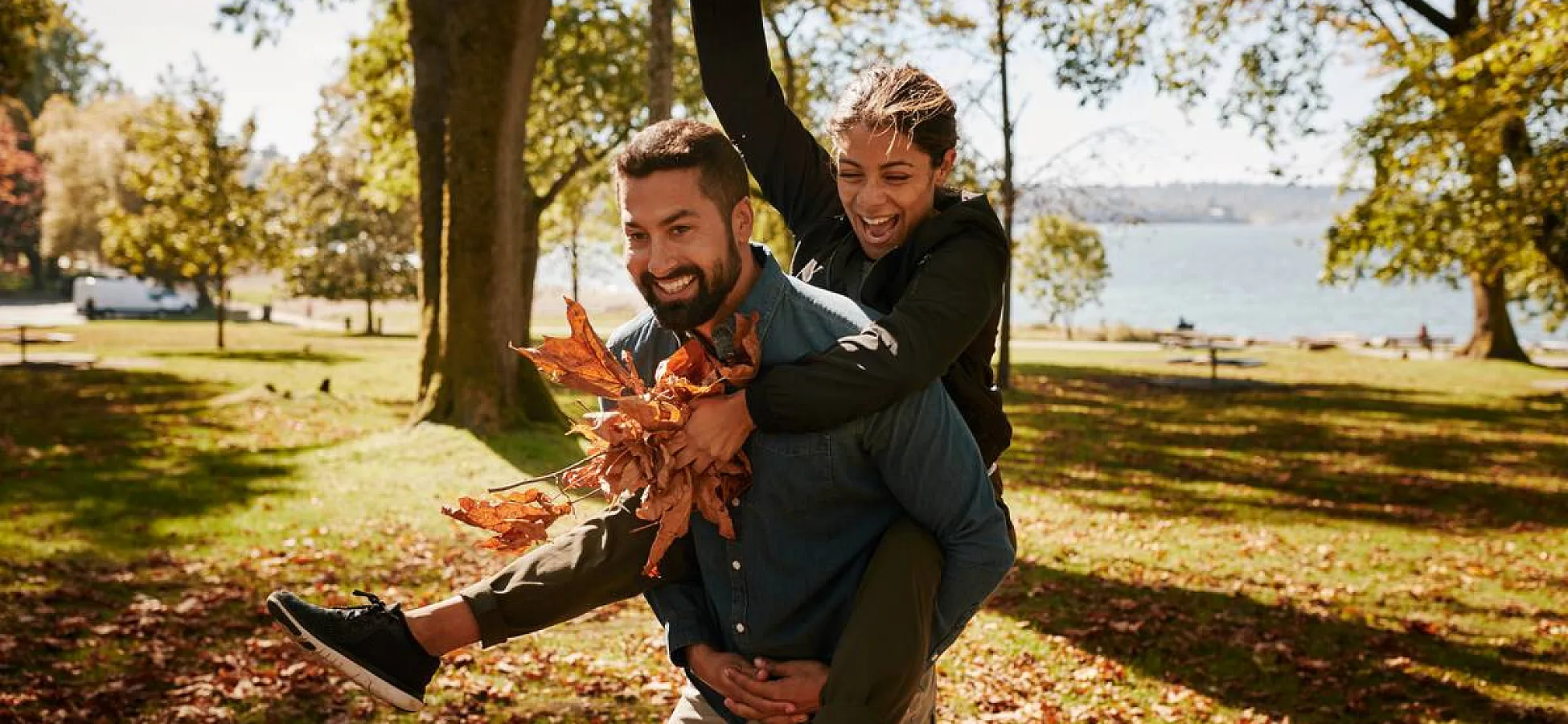 Couple playing in the park with autumn leaves. There are crisp golden leaves sprinkling the grass with the ocean in the background.