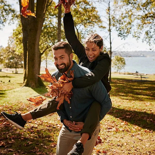 Couple playing in the park with autumn leaves. There are crisp golden leaves sprinkling the grass with the ocean in the background.