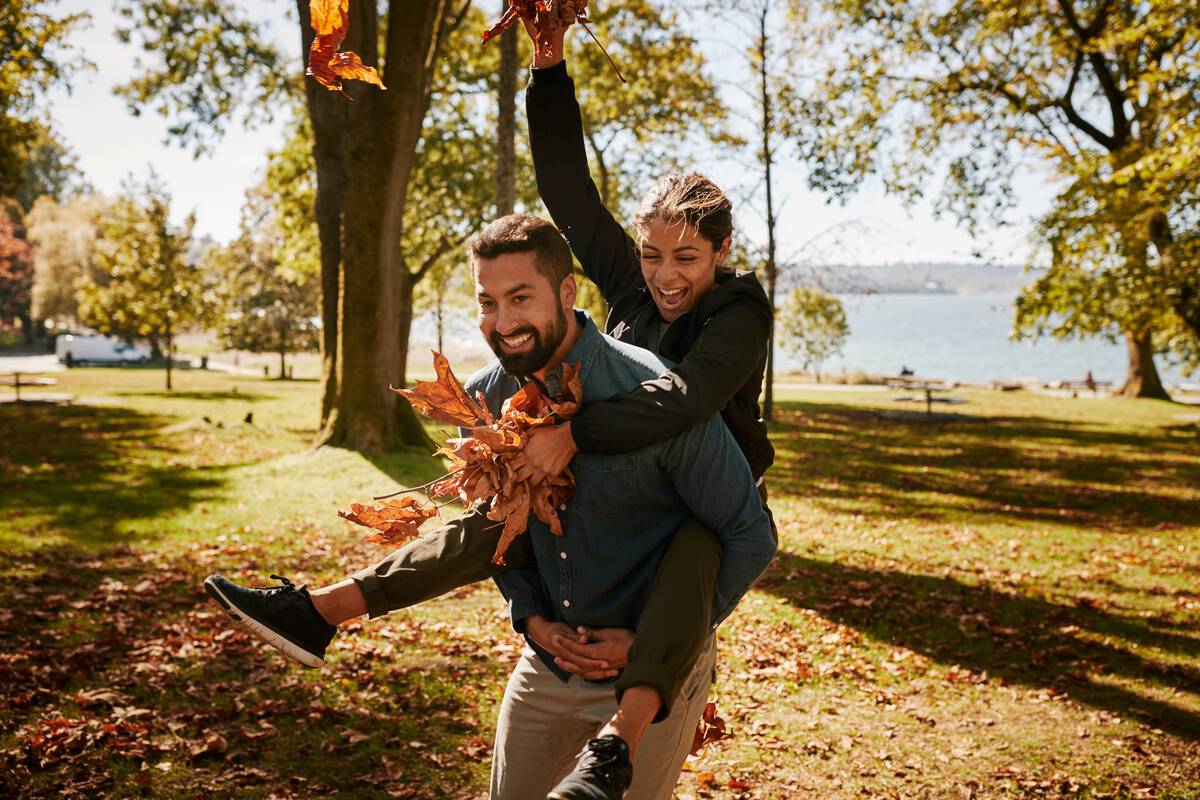 Couple playing in the park with autumn leaves. There are crisp golden leaves sprinkling the grass with the ocean in the background.