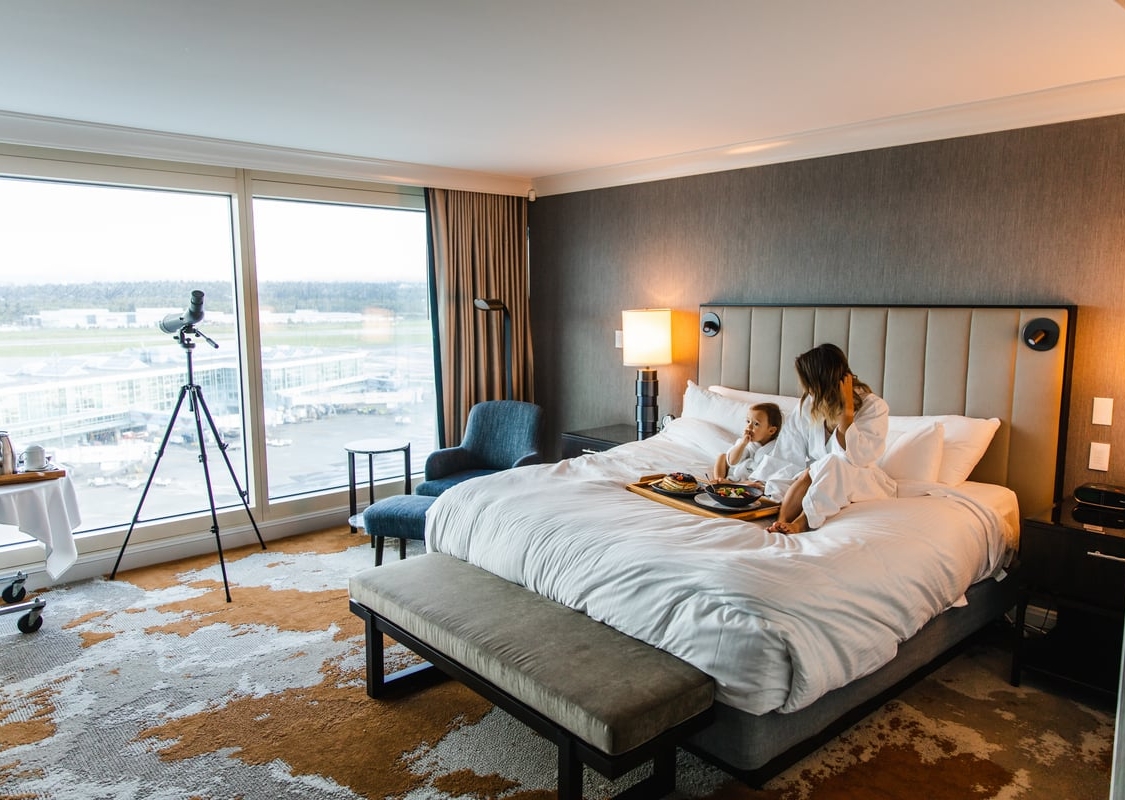 A mom and her child sit in bathrobes on a bed in a hotel