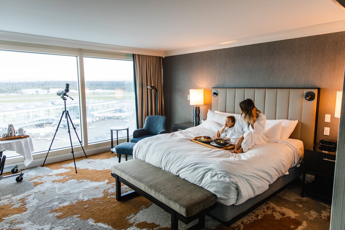 A mom and her child sit in bathrobes on a bed in a hotel