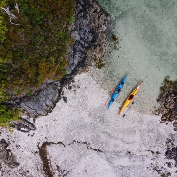 A bird-eye view of two kayaks on a beach, one blue, one yellow, in the Broken Islands Group.