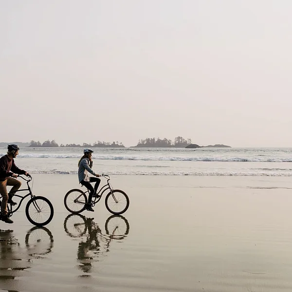 Couple riding bikes along the sand with the ocean and small islands off the coast behind them