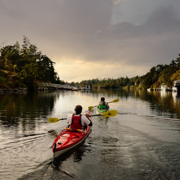 Two people are kayaking down a river at sunset