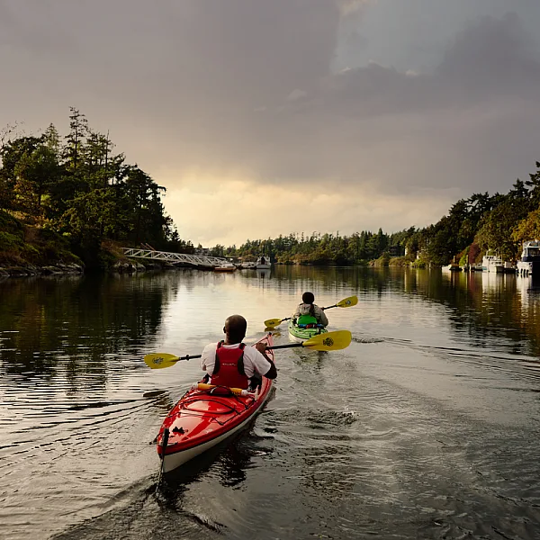 Zwei Personen fahren mit dem Kajak einen Fluss hinunter bei Sonnenuntergang