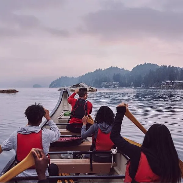 A group of people paddle a large wooden canoe on the ocean.