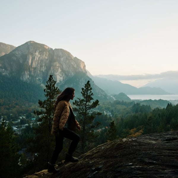 A person hikes along a granite rockface with views of Howe Sound and the Stawamus Chief monolith.