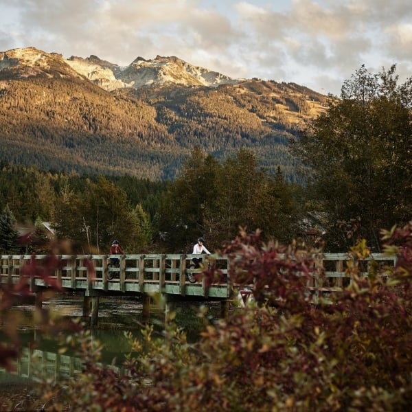 Dos mujeres andan en bicicleta por un puente en Green Lake, Whistler.