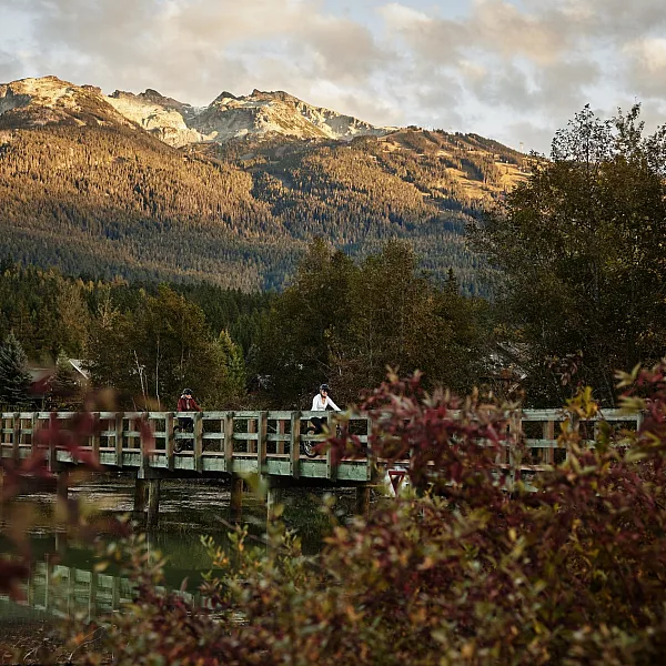 Dos mujeres andan en bicicleta por un puente en Green Lake, Whistler.