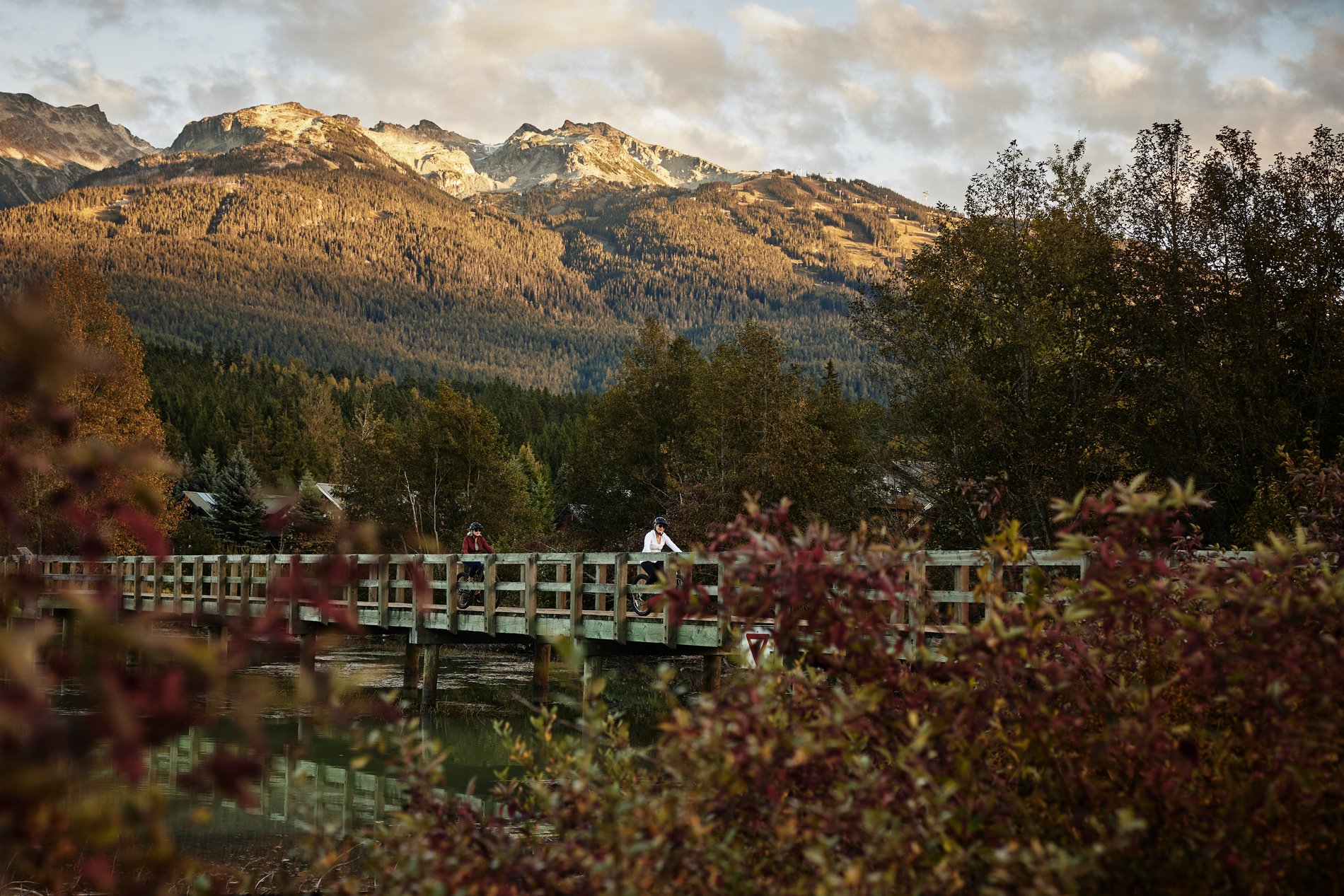 Two women cycle across a bridge at Green Lake, Whistler