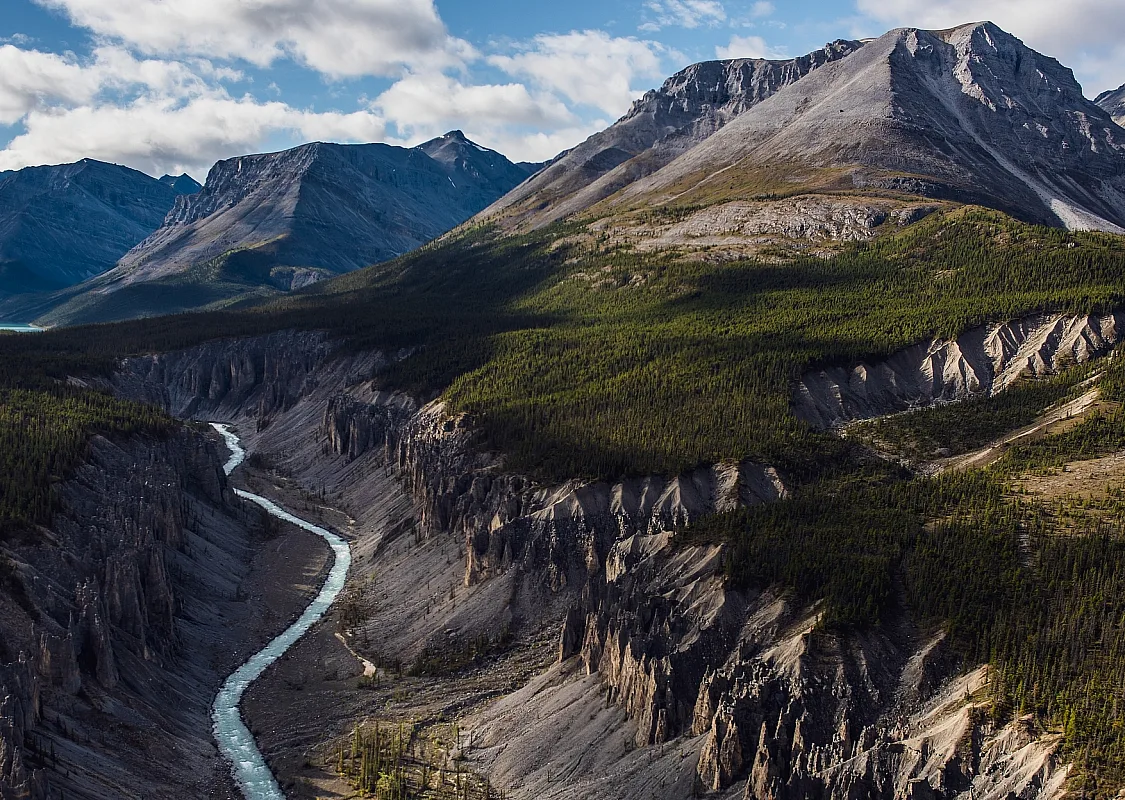 Rugged mountains tower over a valley with lush forest and a river.