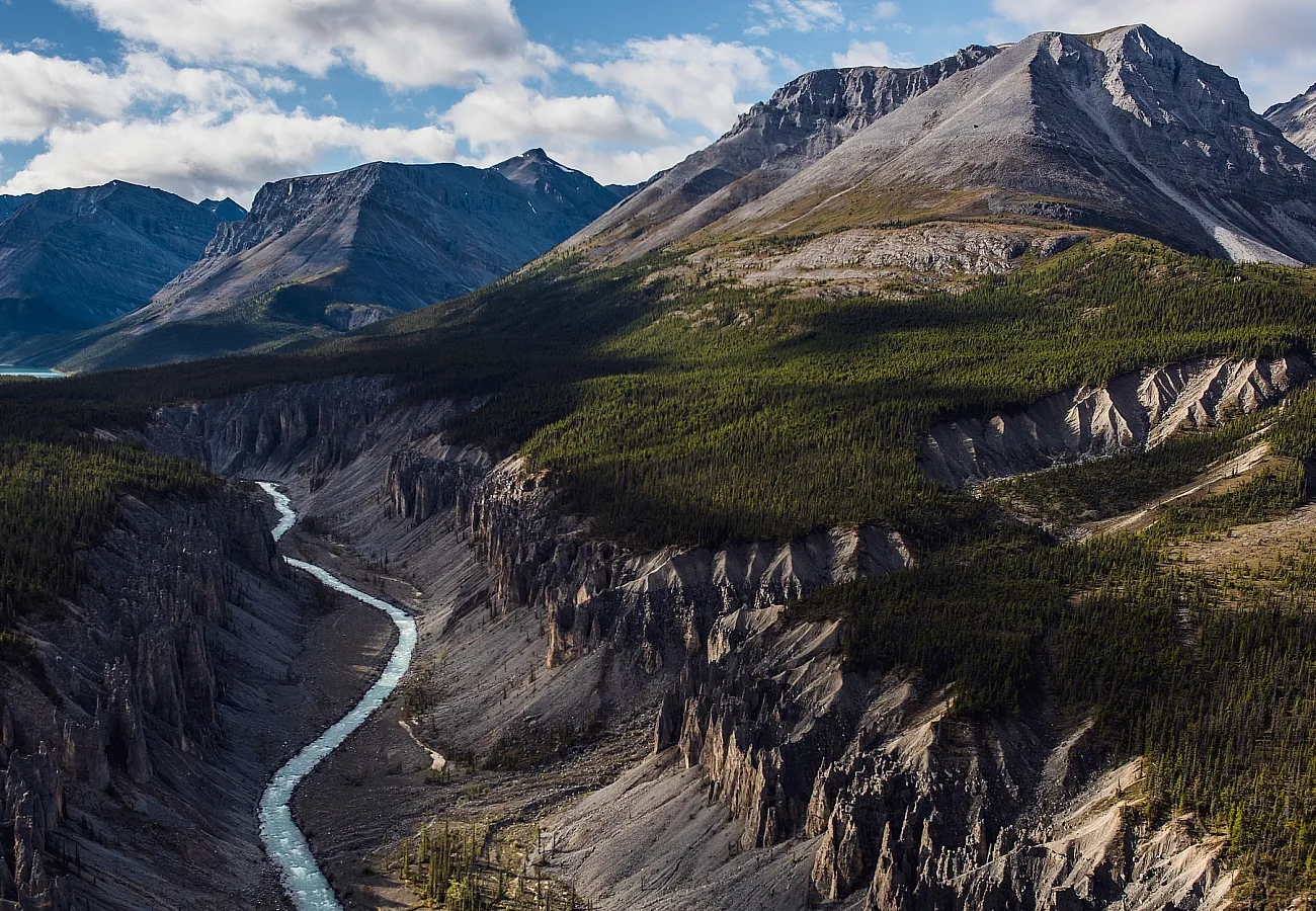 Rugged mountains tower over a valley with lush forest and a river.