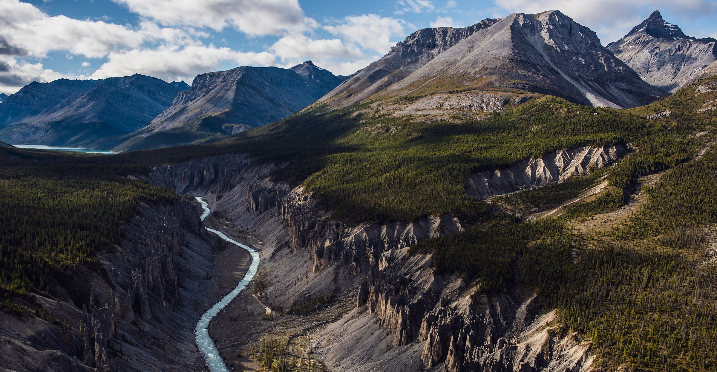 Rugged mountains tower over a valley with lush forest and a river.