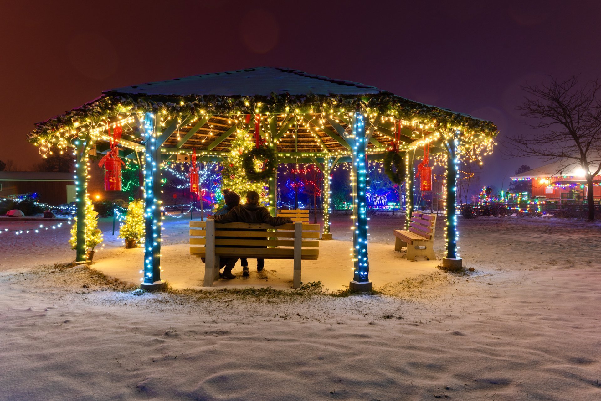 Couple sitting on a bench in a gazebo decorated with Christmas lights at the BC Wildlife Park in Kamloops | Peter Olsen