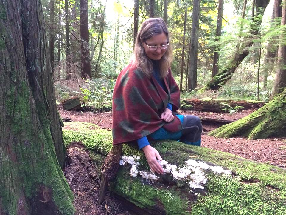 Haida Bolton leans over a patch of mushrooms growing on a fallen tree in the forest in Pender Harbour