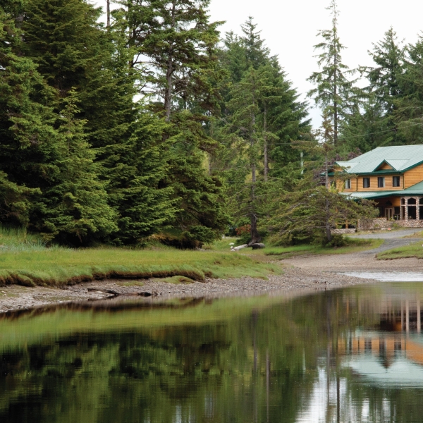 Outside of Haida House seen between the trees. The building reflects of the lakes edge.