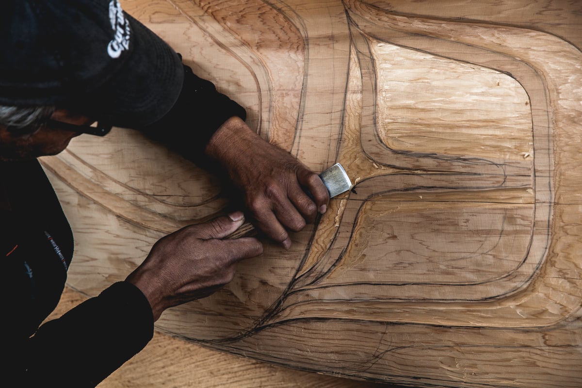 A person is holding a carving tool on a large piece of wood.