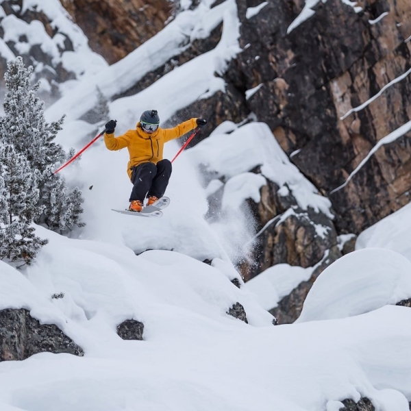 Una persona salta de una roca grande con esquís en Kicking Horse Mountain Resort.