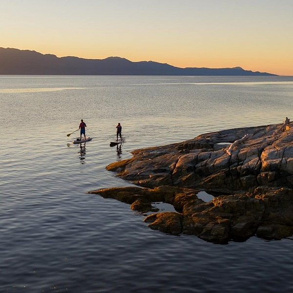 Two people paddleboard off a rocky shoreline.