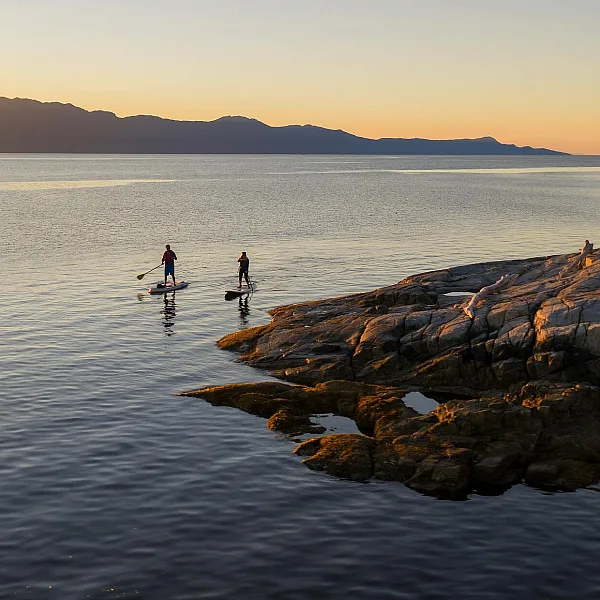 Two people paddleboard off a rocky shoreline.