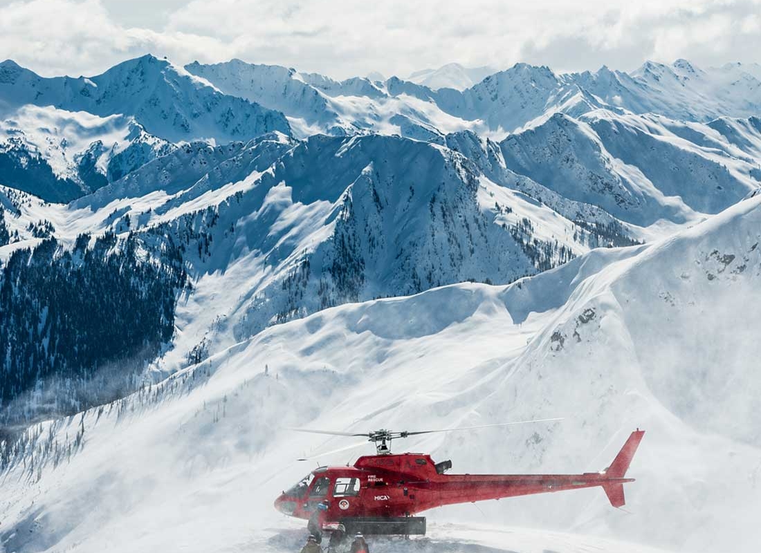 Grupo de esquiadores de heliesquí siendo recogidos por un helicóptero cerca de Mica Heli Skiing Lodge.
