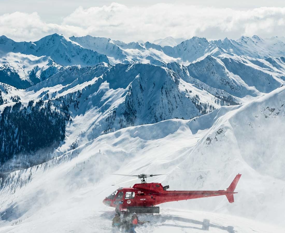 Grupo de esquiadores de heliesquí siendo recogidos por un helicóptero cerca de Mica Heli Skiing Lodge.
