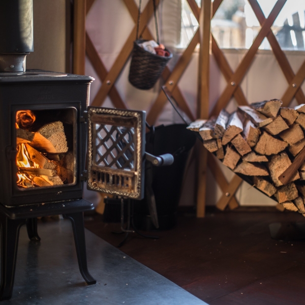 A wood burning fire and a stack of firewood against the wall inside a yurt