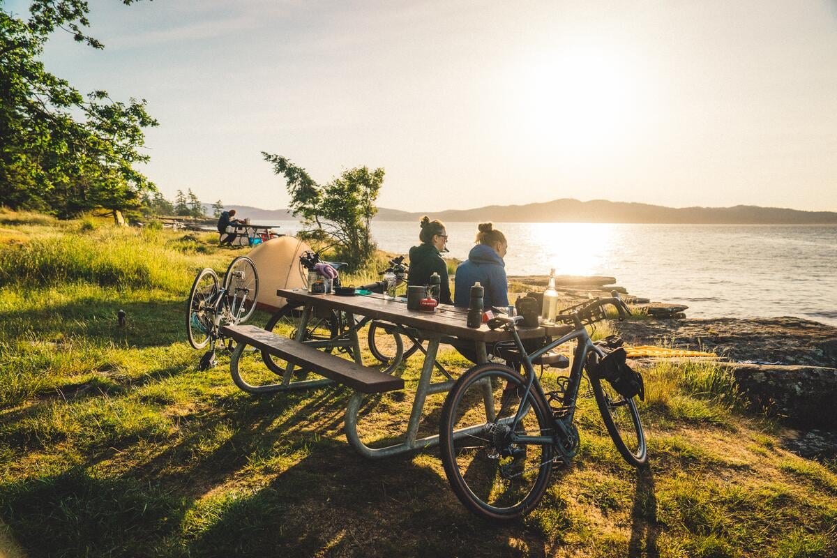 Two people sitting at a picnic table enjoying the ocean view at Ruckle Provincial Park during a bikepacking trip on Salt Spring Island.
