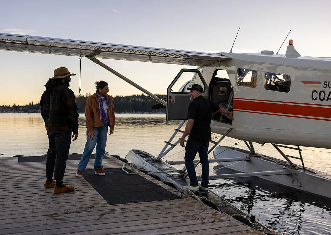 Three people stand beside a seaplane at a wooden dock.