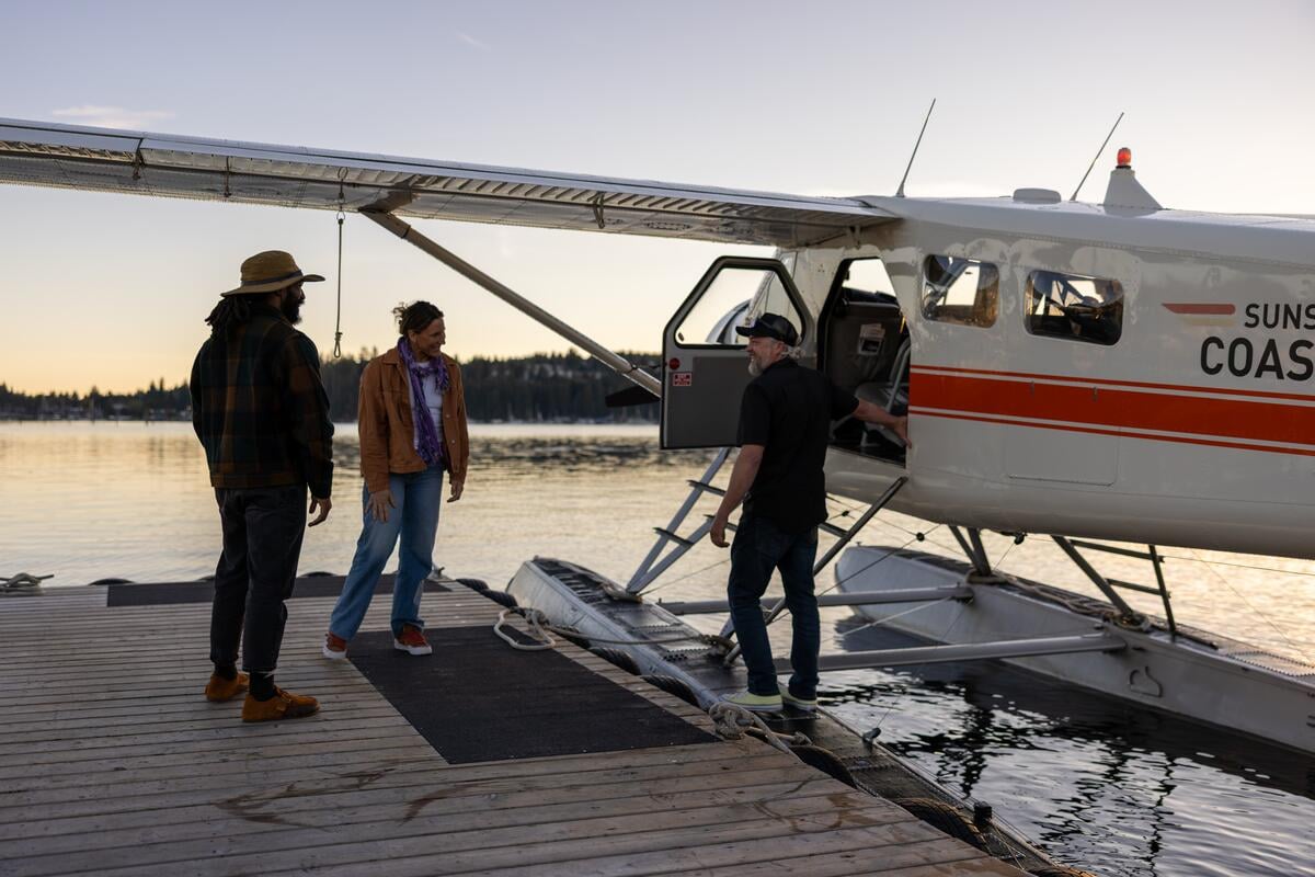 Three people stand beside a seaplane at a wooden dock.