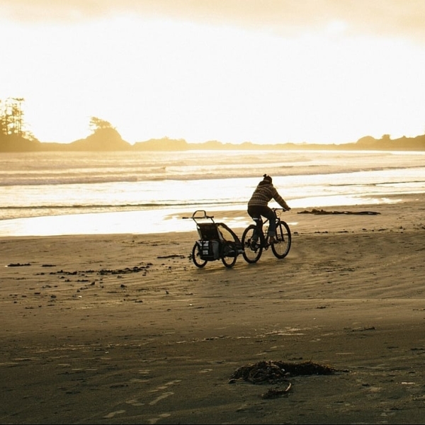 A person on a bike pulls a trailer long the beach.