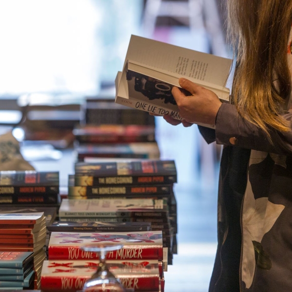 Woman standing and thumbing through a novel at a table full of many different books.