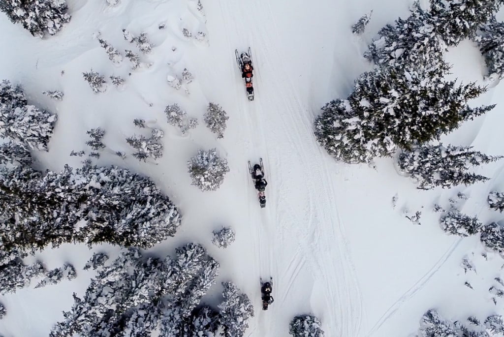 Aerial photograph of three people snowmobiling through a winter terrain in the trees