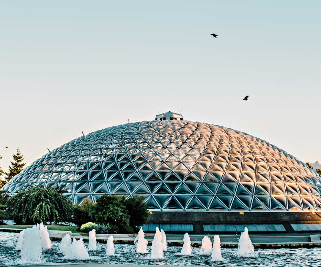 A dozen short fountains flow out of a pool in front of the glass dome of the Bloedel Conservatory