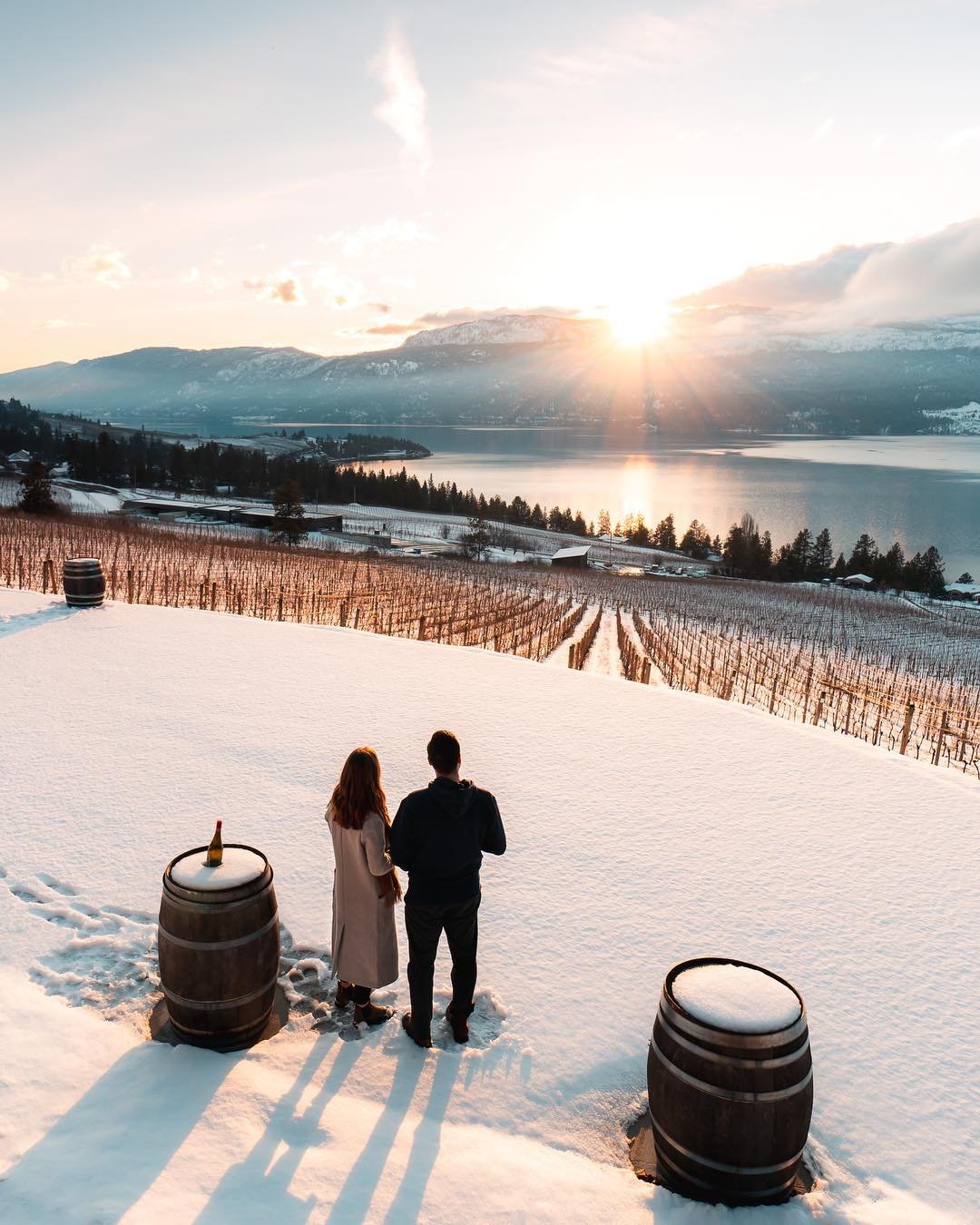 A man and women stand out in the snow together, facing out towards the vineyard and the lake at 50 Parallel Estate Winery