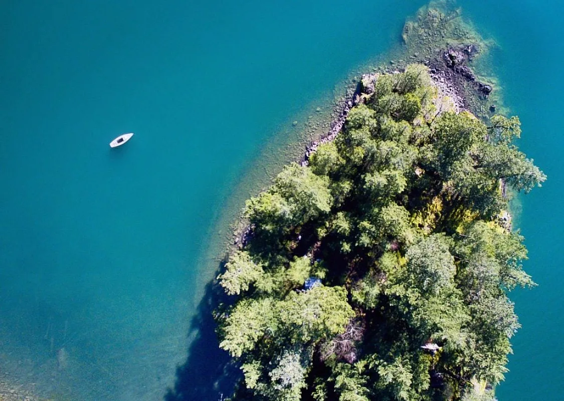 Aerial photo of a tree covered island surrounded by a bright blue lake with a kayak