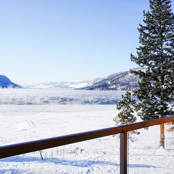 Verschneite Aussicht von der Terrasse der Quaaout Lodge mit Blick auf ein weites, leeres Feld und Berge in der Ferne.