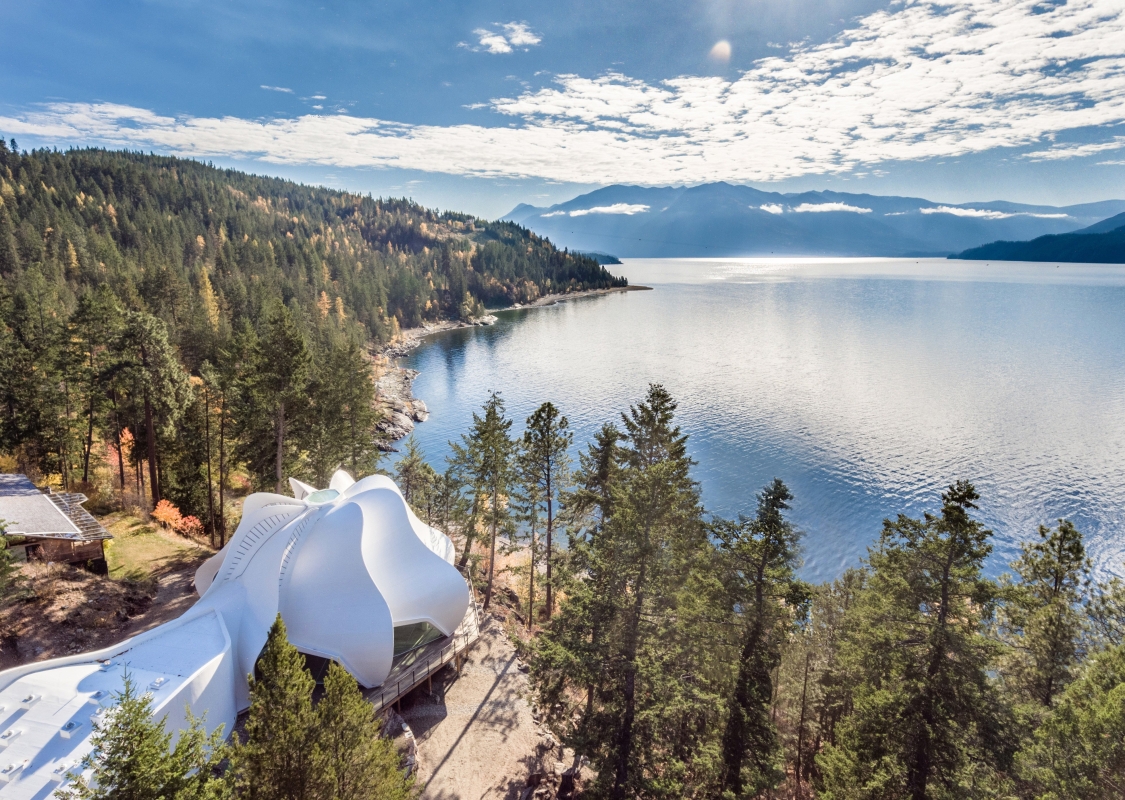 A white domed building the Yasodhara Ashram, sits next to a lake surrounded by trees.