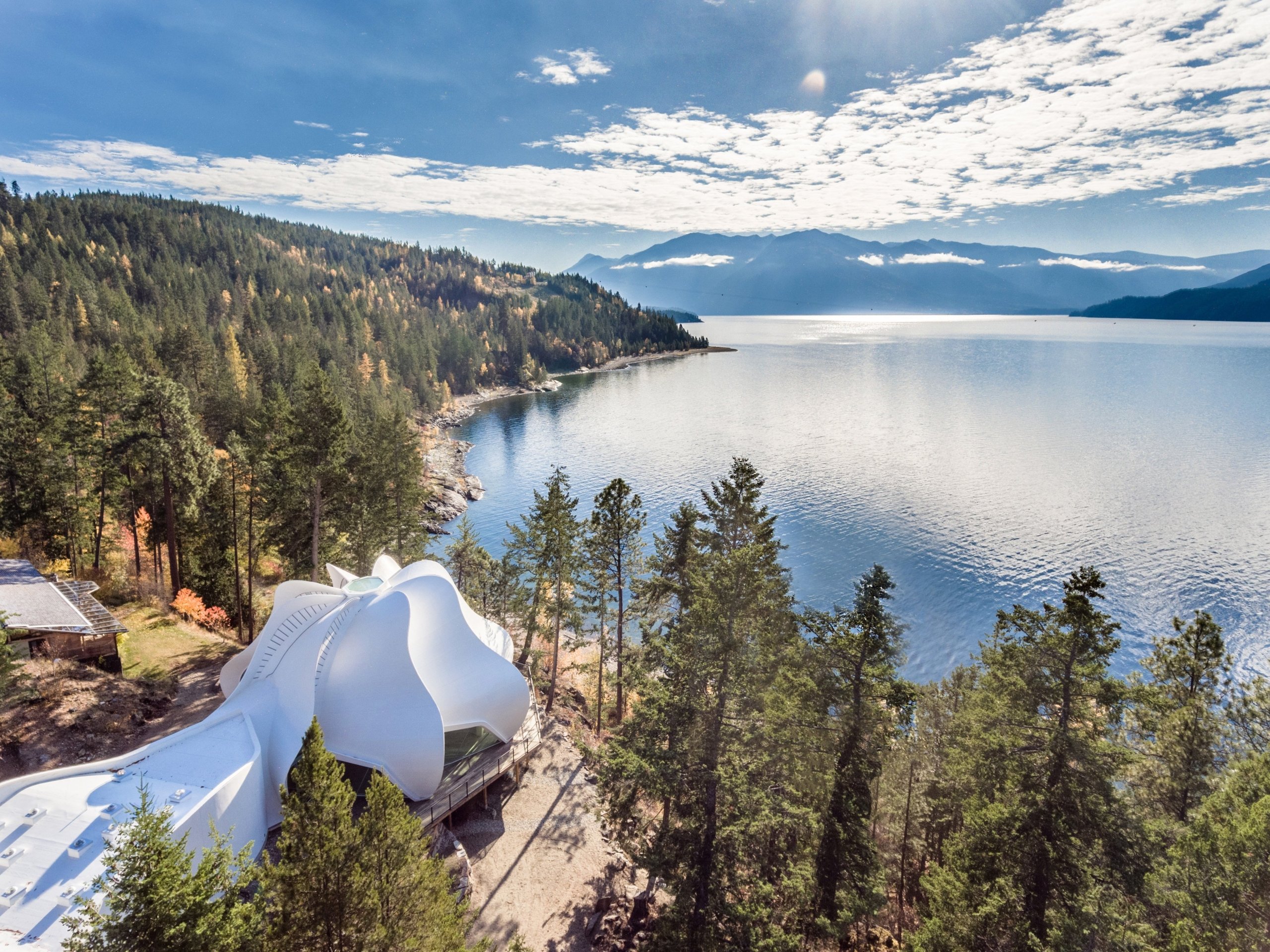 A white domed building the Yasodhara Ashram, sits next to a lake surrounded by trees.
