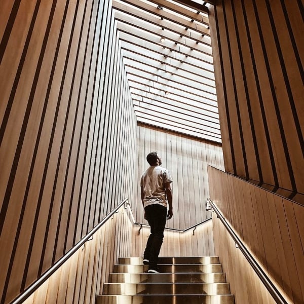 A man looks up at the wood slat ceiling from the top of a staircase inside the Audain Art Museum